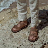 Rory Brown Crust Leather Mules with Metal Buckles, styled with beige linen trousers - POEVE Collection