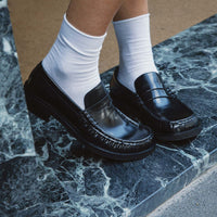 Vera Black Brushed Leather Loafers, styled with crisp white socks and worn on green-veined marble steps - POEVE Collection
