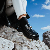 Myte Black Brushed Leather Loafers with Metal Buckle, styled with black socks and white cuffed trousers - POEVE Collection