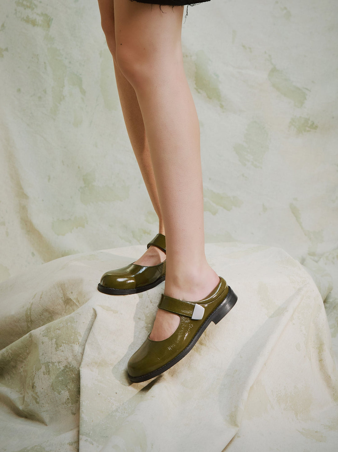 Maris Green Crinkled Patent Leather Mule, styled with a short black textured skirt - POEVE Collection