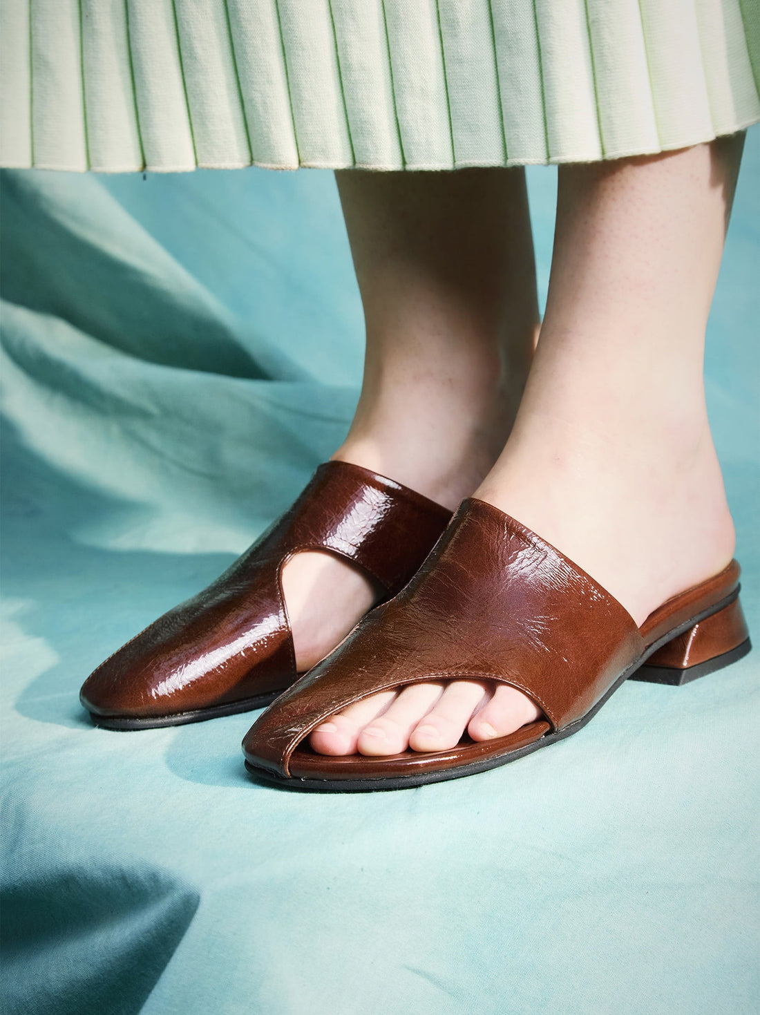 Melanie Brown Crinkled Patent Leather Mules, styled with a mint green pleated skirt - POEVE Collection