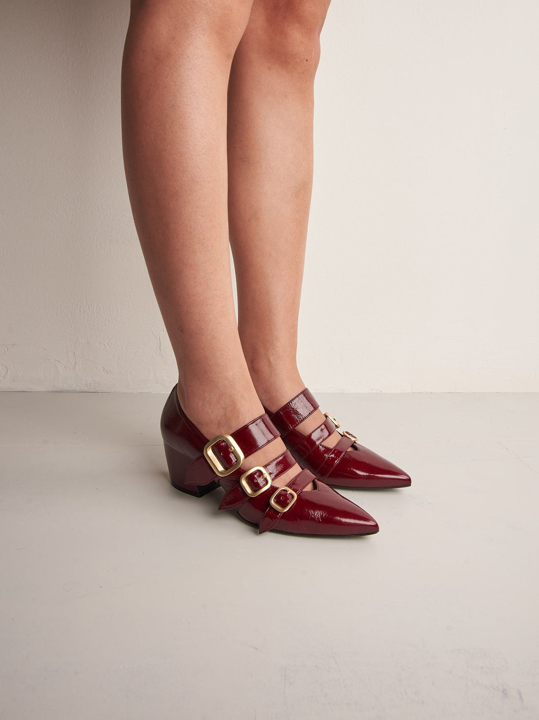 Nova Cherry Red Crinkled Patent Leather Heel Shoes with Metal Buckles, worn on bare legs - POEVE Collection