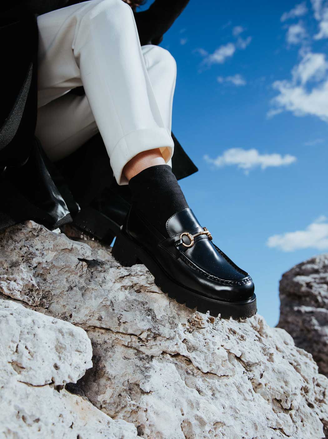 Myte Black Brushed Leather Loafers with Metal Buckle, styled with black socks and white cuffed trousers - POEVE Collection